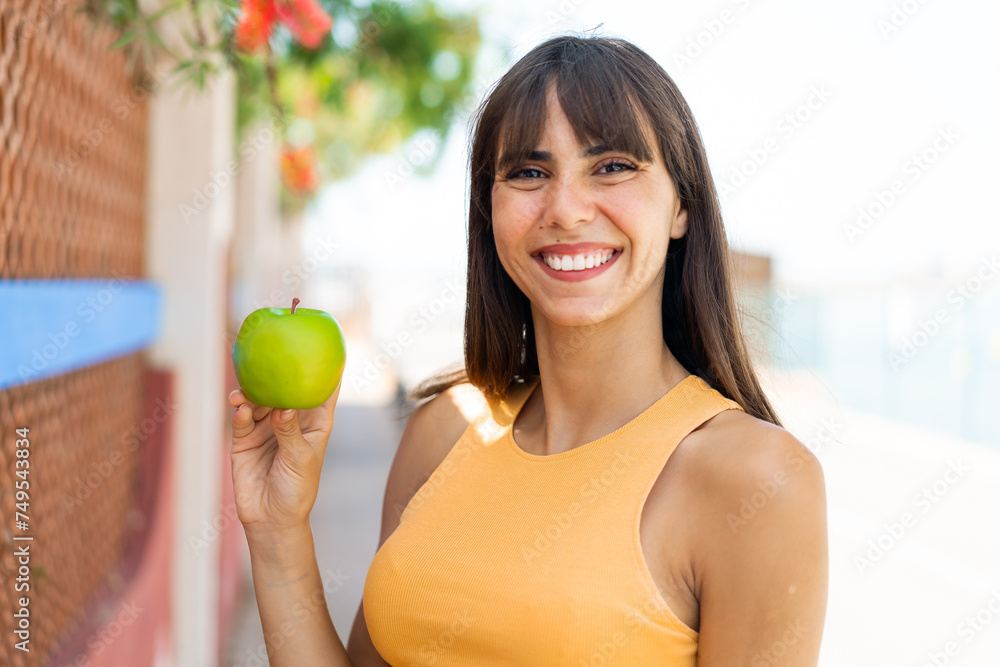 Young woman with an apple at outdoors smiling a lot Young woman with an apple at outdoors smiling a lot