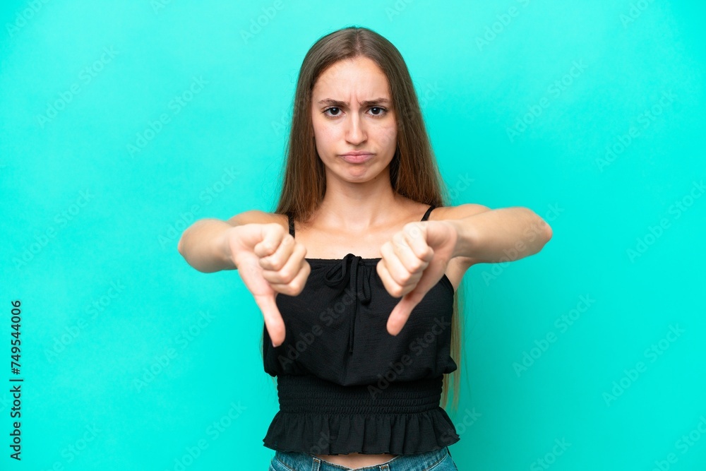 Fototapeta premium Young caucasian woman isolated on blue background showing thumb down with two hands