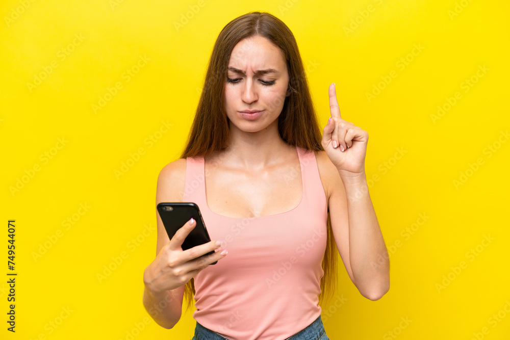 Young caucasian woman isolated on yellow background using mobile phone and lifting finger Young caucasian woman isolated on yellow background using mobile phone and lifting finger