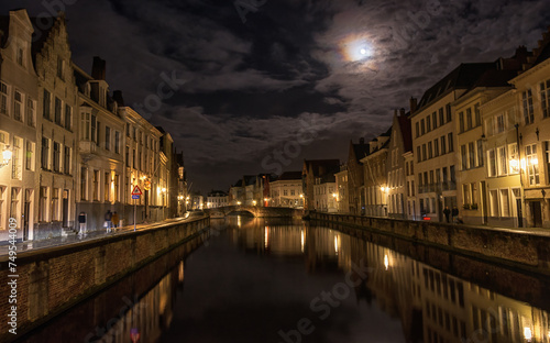 Night shot of old canals and buildings in the medieval Flemish city of Bruges. View of the canals and the night city of Bruges, which is beautifully illuminated by the full moon. © leesle