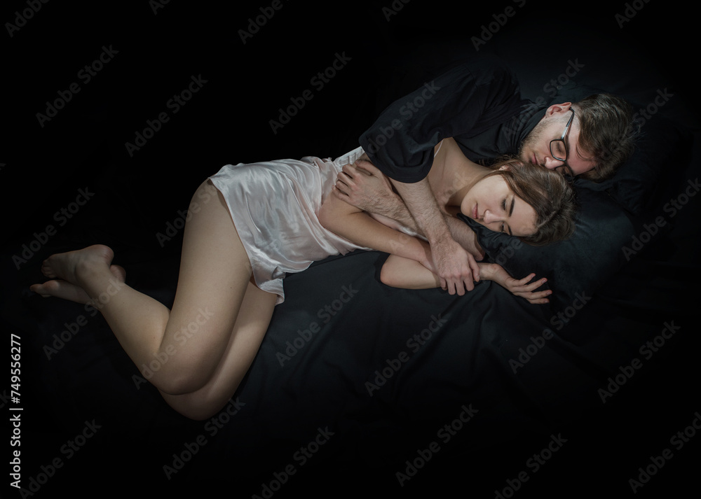 A young couple in love lies hugging on a dark background. A young couple in love lies hugging on a dark background.