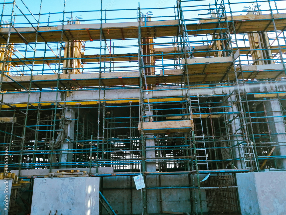A building under construction with scaffolding and a sign on the scaffolding. The building is tall and has a lot of scaffolding around it