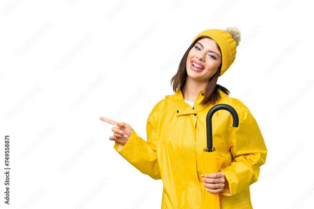 Young Russian woman with rainproof coat and umbrella over isolated chroma key background pointing finger to the side and presenting a product Young Russian woman with rainproof coat and umbrella over isolated chroma key background pointing finger to the side and presenting a product