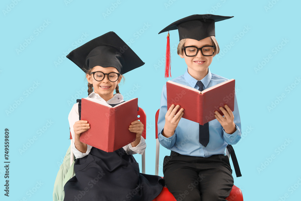 Little children in graduation hats reading books on blue background. End of school year Little children in graduation hats reading books on blue background. End of school year