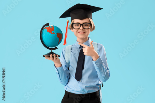 Little boy in graduation hat pointing at globe on blue background. End of school year