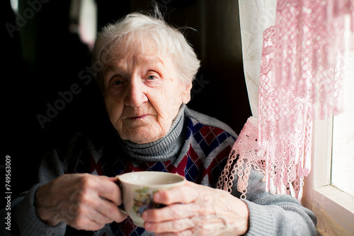Portrait of an elderly woman drinking tea at a table.