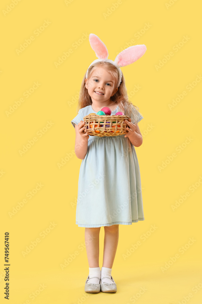 Little girl in bunny ears with Easter eggs on yellow background