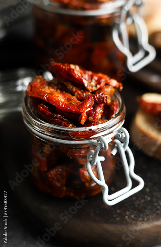 Sun-dried tomatoes in a glass jar. Tomatoes with spices. Dark background. Summer dish. Italian cuisine.
