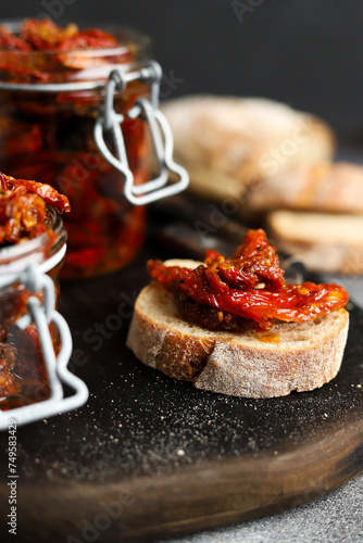 Sun-dried tomatoes in a glass jar. Tomatoes with spices. Dark background. Summer dish. Italian cuisine. Sun-dried tomatoes on white bread.