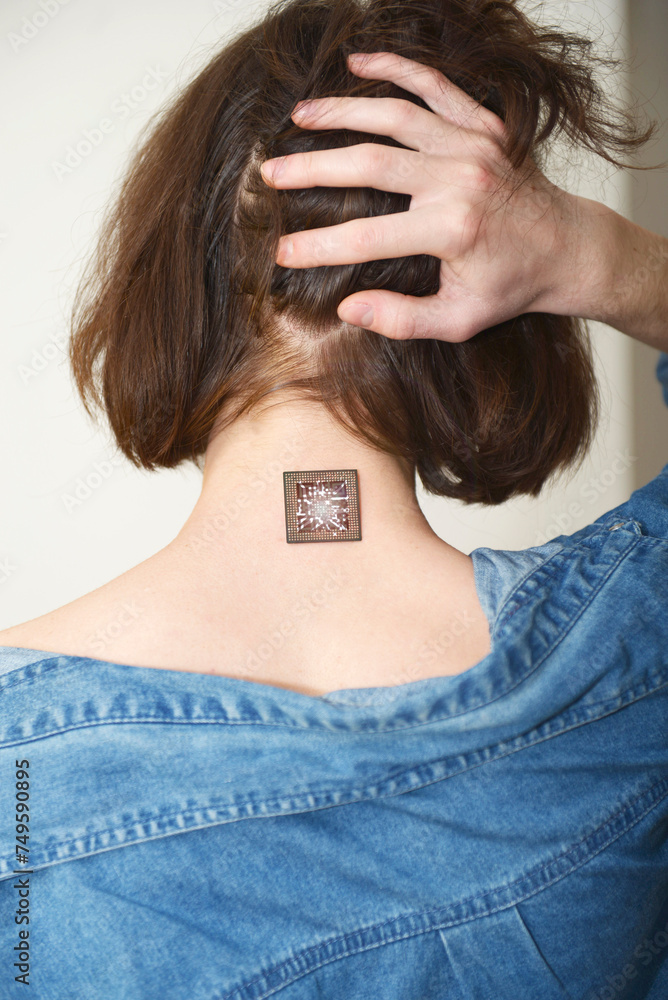 A man shows a microcircuit chip on his neck, holding up his hair. A ...