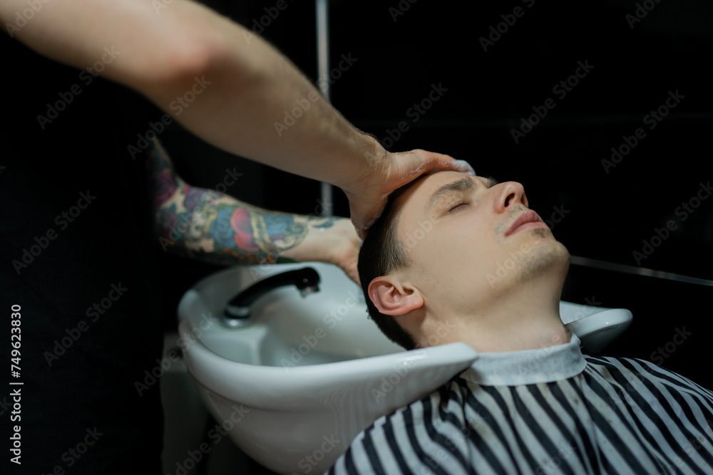A barber man with a tattoo on his arm makes a haircut to a brunette guy in a barbershop, cuts his hair with a clipper close-up A barber man with a tattoo on his arm makes a haircut to a brunette guy in a barbershop, cuts his hair with a clipper close-up