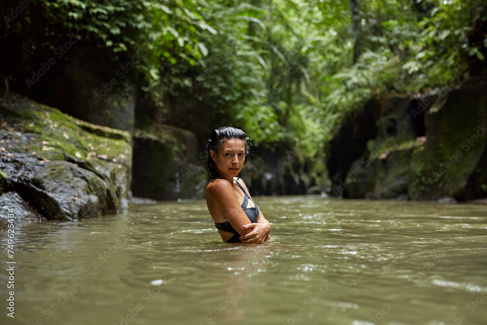A young slender woman in a swimsuit poses by a mountain river in the jungle on the popular island of Bali. A young slender woman in a swimsuit poses by a mountain river in the jungle on the popular island of Bali.