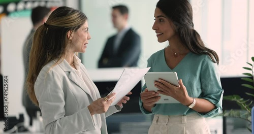 Two young attractive businesswomen colleagues discuss contract details, smile, enjoy conversation walk along hallway in modern office, share ideas, opinion, solutions, engaged in teamwork and workflow