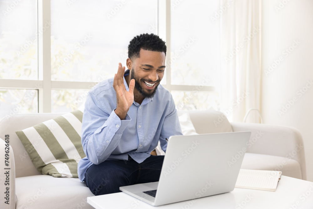 Happy African American student guy enjoying online conversation at laptop, waving hand hello, smiling, laughing, using Internet technology connection for education, teaching, communication on Internet Happy African American student guy enjoying online conversation at laptop, waving hand hello, smiling, laughing, using Internet technology connection for education, teaching, communication on Internet