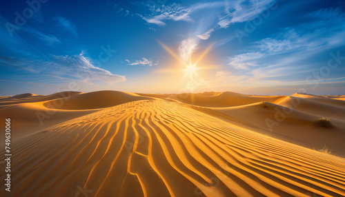The sun sets over a desert, casting long shadows and warm light on the sand dunes under a sky streaked with clouds