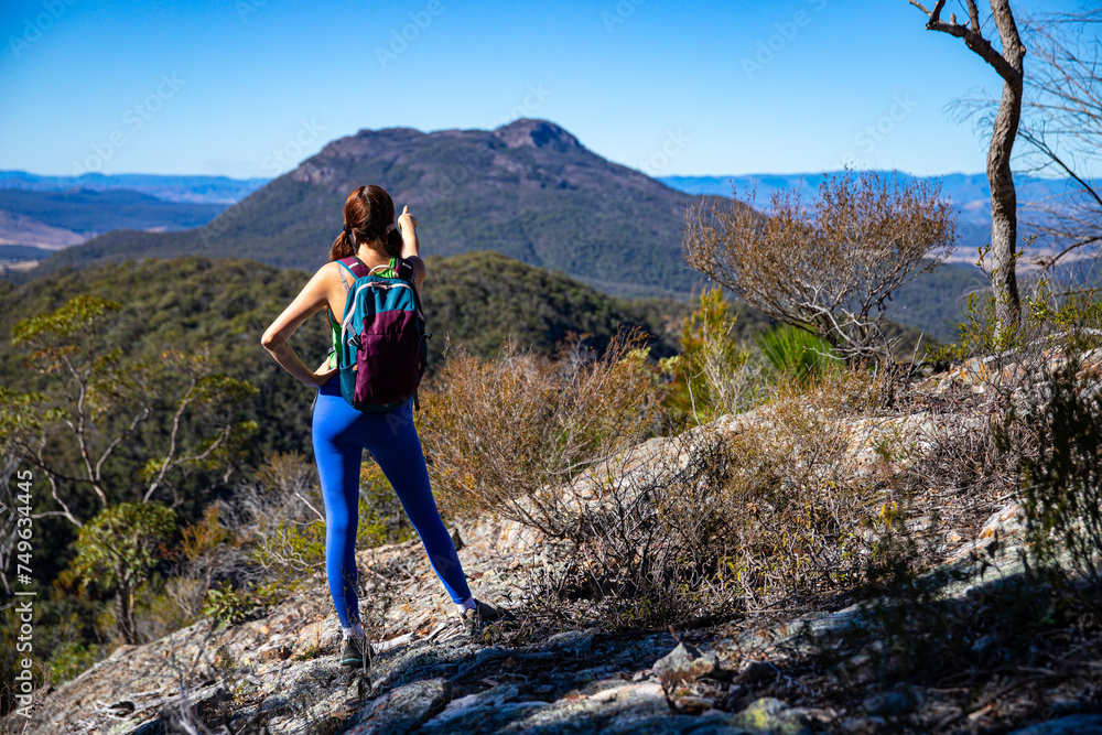 Obraz premium hiker girl looking at the peak of mount maroon from the top of mount may in mount barney national park, south east queensland, australia