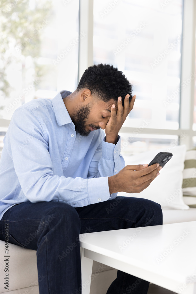 Tired frustrated young African man having problems with mobile phone, bad connection, online communication failure, application error, touching head with closed eyes