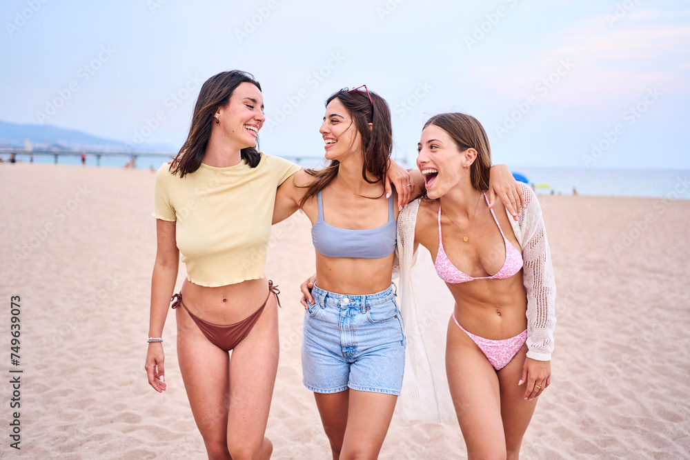 Group of Happy caucasian girl friends in bikini enjoying vacation at the beach outdoors. Walking in the sand and laughing a lot by the sea in a sunny day with swimwear celebrating carefree