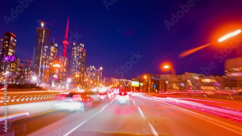 Bright long exposure motion hyperlapse of a speed driving in Toronto, Ontario, Canada. Speedy car front POV view at the highway with a lot of traffic lights stricks. Passing by city downtown buildings photo