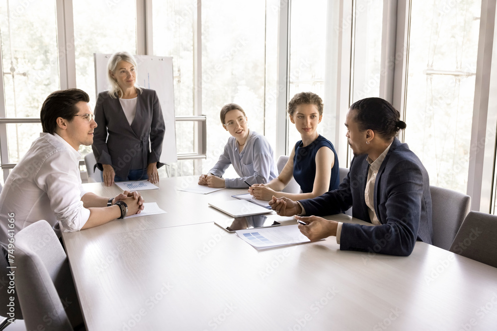 Marketing department gathered together at meeting led by mature female boss, review sales results, discuss project, solve issues share vision and professional opinion sit at desk in conference room Marketing department gathered together at meeting led by mature female boss, review sales results, discuss project, solve issues share vision and professional opinion sit at desk in conference room