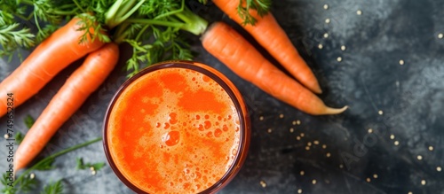 A clear glass filled with freshly squeezed carrot juice is placed amid a bunch of vibrant orange carrots. The carrots are scattered around the glass, highlighting the freshness and health benefits of