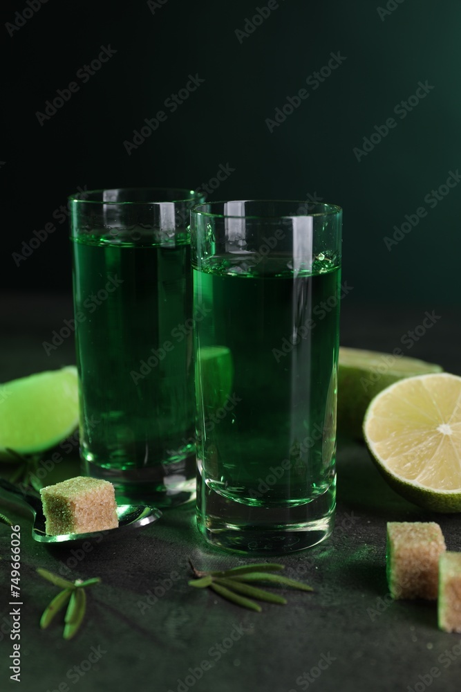 Fototapeta premium Absinthe in shot glasses, spoon, brown sugar, lime and rosemary on gray table. Alcoholic drink