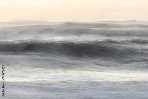 The image is a blurry shot of a wave crashing on a beach © wollertz