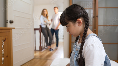 Stressed and unhappy young girl huddle in corner, cover her ears blocking sound of her parent arguing in background. Domestic violence at home and traumatic childhood develop to depression. Synchronos