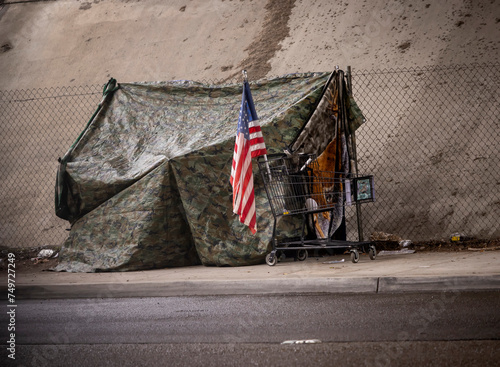 An American flag at a homeless tent made of camouflage tarp at a road underpass photo