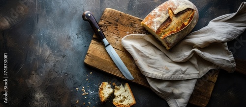 A piece of whole grain bread is placed on a wooden cutting board next to a knife. The bread appears fresh and ready for slicing or serving.