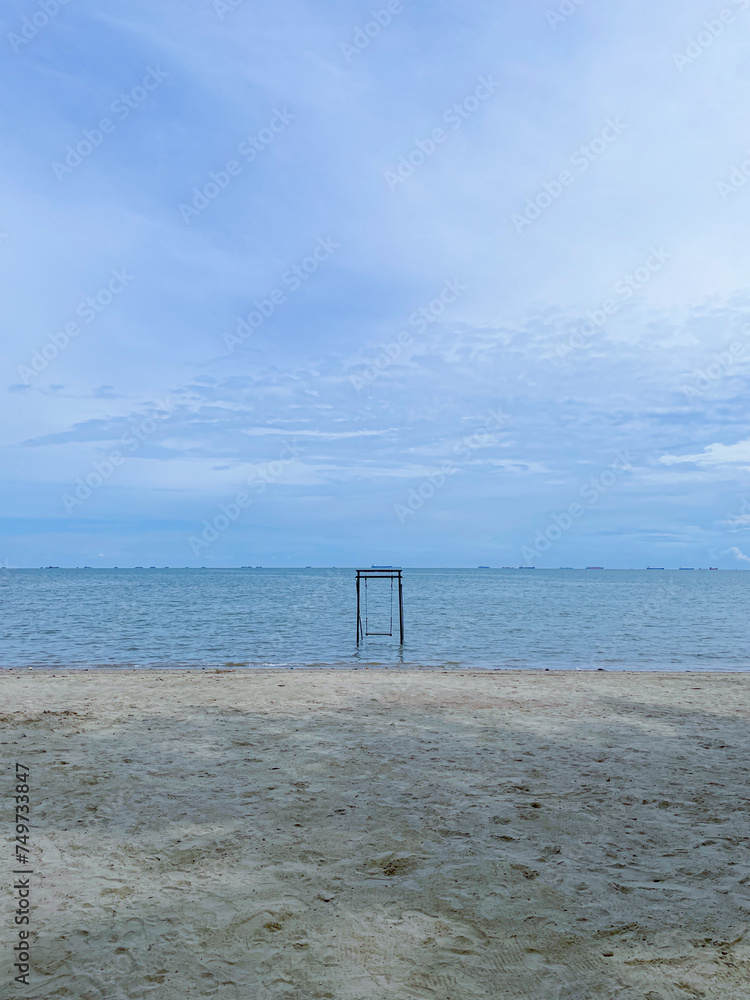 photo of a beach view with a cloudy sky and a swing in the middle of the beach