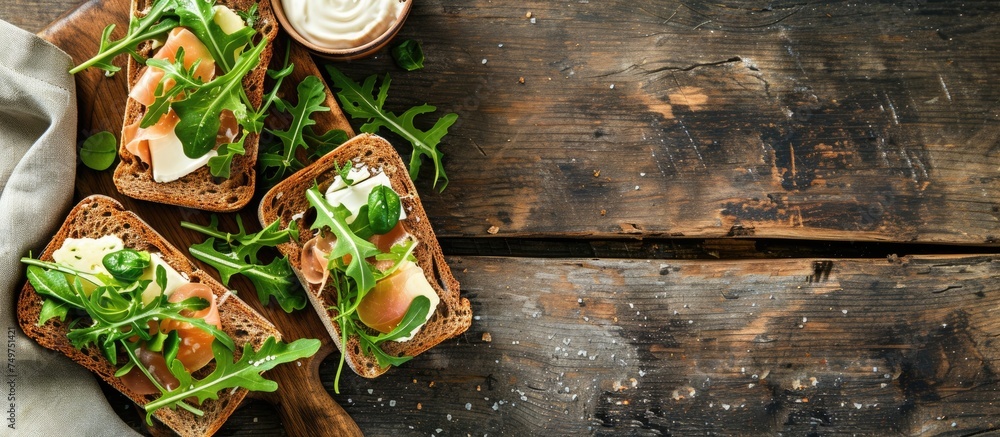A variety of food items including healthy wholegrain brown bread with ham, cheese, watercress, and salad greens served on a chopping board on a rustic wooden table. The food is accompanied by a side