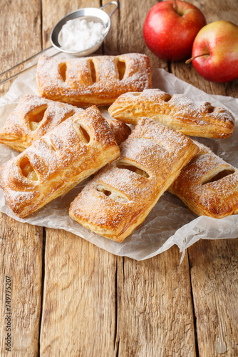 Freshly baked puff pastry with apples on baking paper close-up on a wooden table. Vertical