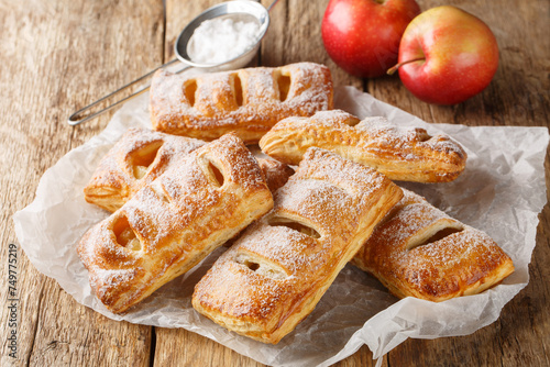 Freshly baked apple puff pastries with powdered sugar close-up on a paper wooden table. Horizontal © FomaA