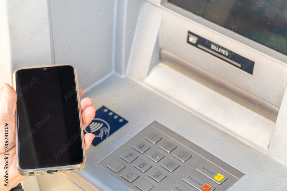 Older woman brings the phone to the ATM, NFC contactless communication concept Older woman brings the phone to the ATM, NFC contactless communication concept