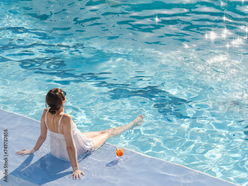 Cute woman with a glass of drink sits near the swimming pool of a cruise ship. Sunny, clear morning. View from above. Closeup, outdoors. Vacation and travel concept