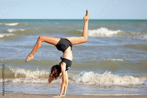 girl does a cartwheel with her hands on the beach and legs in the air on the seashore in summer