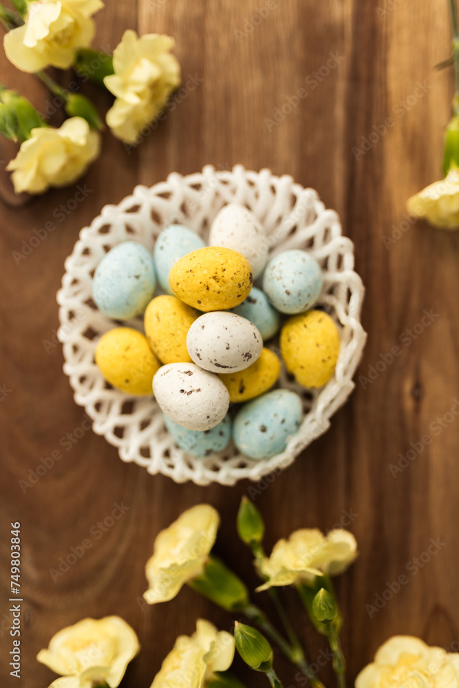 Yellow flowers and pastel yellow and blue colored eggs in a white small wicker basket on a background of brown wood. Layout. Mockups. Pastel Springs background. Easter background. Easter eggs close up Yellow flowers and pastel yellow and blue colored eggs in a white small wicker basket on a background of brown wood. Layout. Mockups. Pastel Springs background. Easter background. Easter eggs close up