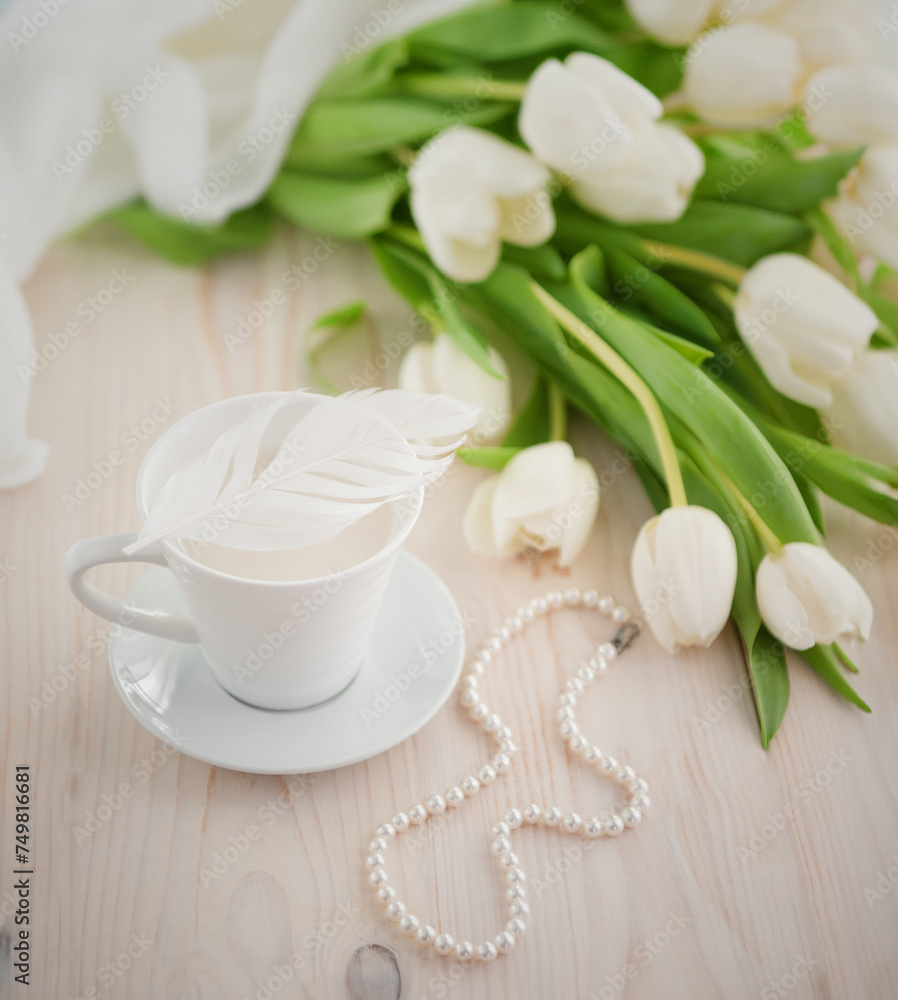 Coffee, white tulips and a feather on a wooden background.
