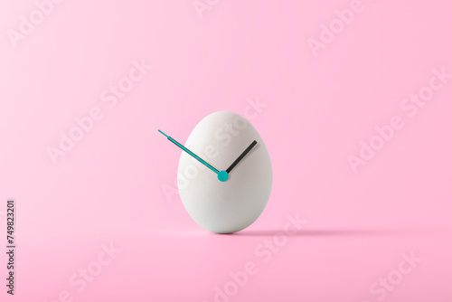 Creative Easter concept. White Easter egg with hour hands on pink background. Easter time.