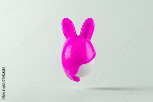 Easter egg with bunny ears painted in pink paint on blue pastel background. Creative Easter concept.