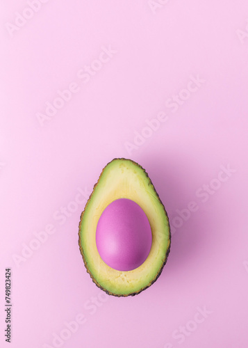 Creative Easter concept. Cut avocado with pink easter egg on pink background with copy space.
