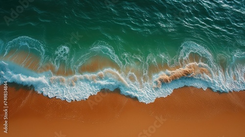 an aerial view of a beach with a wave coming in and a person laying on the sand with their feet in the water.