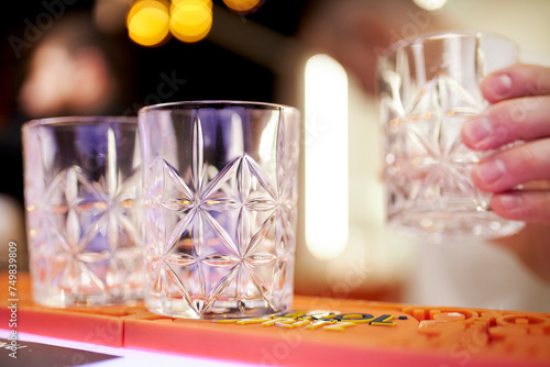 bartender puts an empty faceted glass on the bar counter. Bartender Mixologist Puts Empty Cocktail Glass on Bar Counter. A bartender putting an empty glass with patterns on bar.