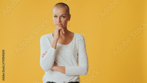 Young hairless woman, thinks over problem, remembering something, looking at camera isolated on yellow background in studio photo