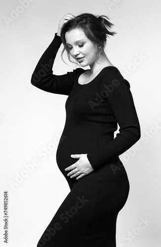 Black and white portrait of pregnant female in black dress with hands near pregnant belly.