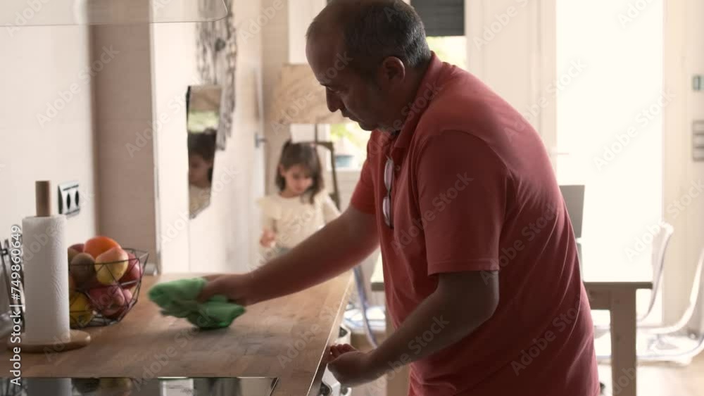 Man cleaning the surface of a kitchen while his granddaughter playing Man cleaning the surface of a kitchen while his granddaughter playing