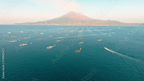 晴れた日の鹿児島湾の青い海と養殖生簀の間を桜島の火山に向かって進む漁船　空撮 photo