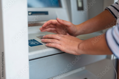 A woman enters a pin code at an ATM. The woman hides her pin with her hand closeup