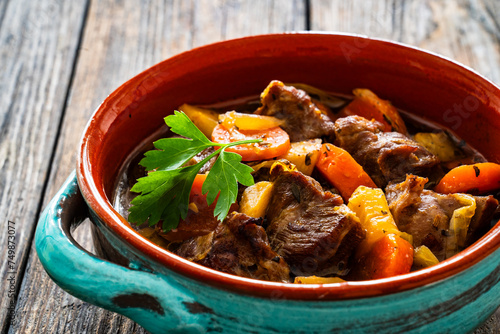 Roast pork cheeks with carrots and celeriac in sauce on wooden table
 photo